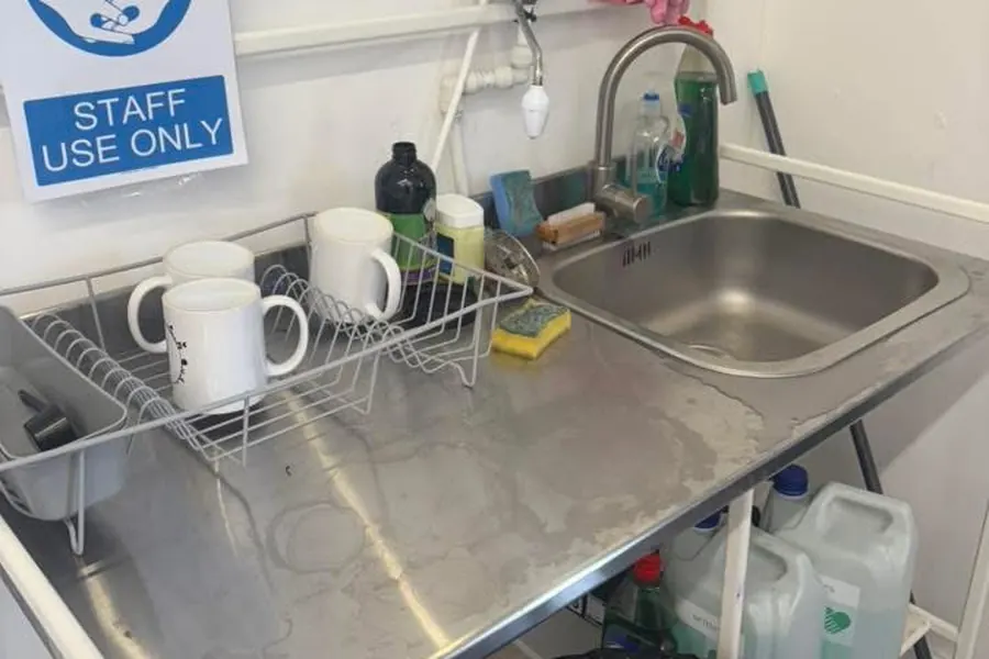 A staff kitchenette before cleaning, worktop covered in mugs and bottles