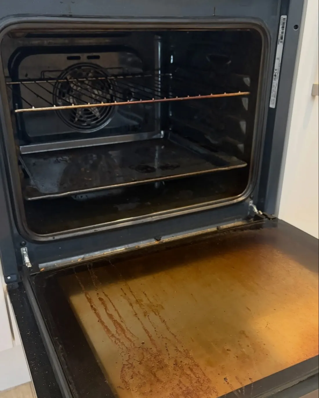 An oven before cleaning, with a stained door and baked on grease